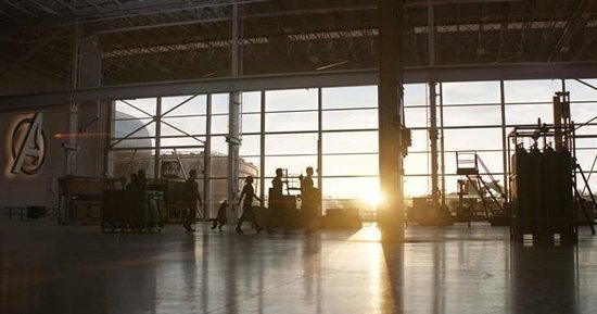 Silhouetten van Avengers die zonsopgang in een hangar bekijken, met het Avengers logo.