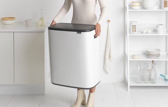 Vrouw draagt de witte Brabantia Bo Touch Bin prullenbak met donkergrijs deksel.