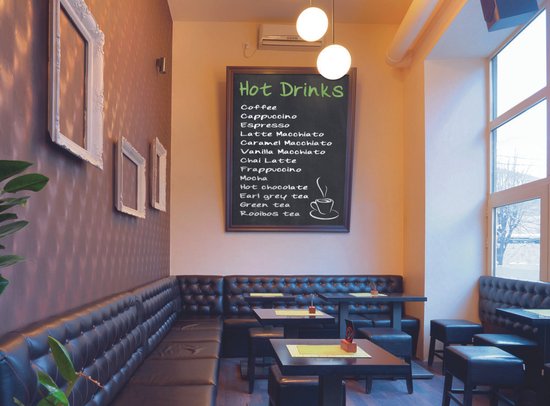 Een café interieur met zwarte leren zitbanken en een krijtbord met 'Hot Drinks' menu.