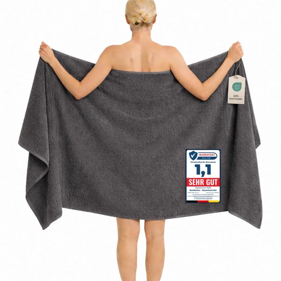 Femme dos à la caméra, portant une grande serviette de bain gris foncé 100% biomatériaux. Une étiquette 'Warentest SEHR GUT' est visible.