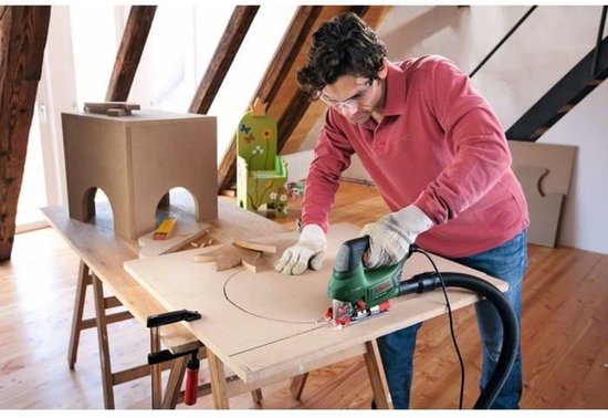 Man met veiligheidsbril en handschoenen zaagt met groene Bosch decoupeerzaag ronding in hout.