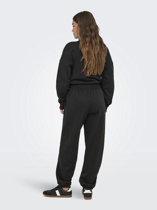Een vrouw met lang bruin haar, van achteren gezien, draagt een zwarte joggingbroek met trekkoord, een bijpassende sweater en sneakers.