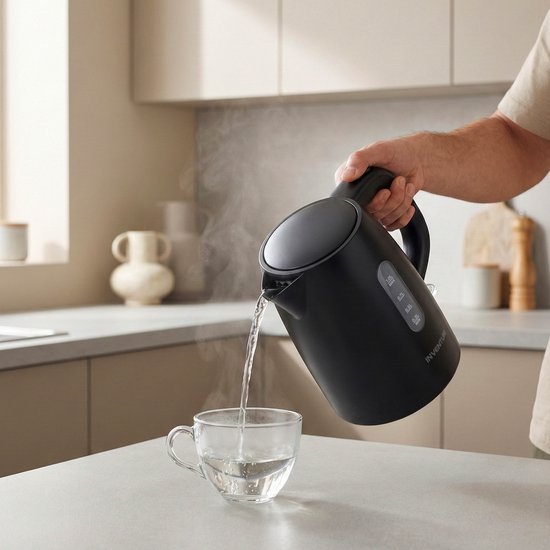 Een hand schenkt kokend water uit de zwarte Inventum waterkoker in een glazen mok.