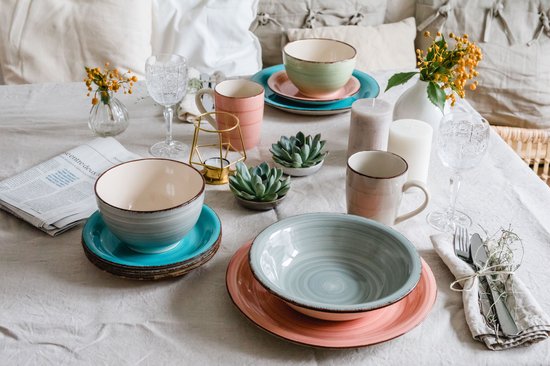 Gedekte tafel met roze, groene en turquoise kommen en bekers.