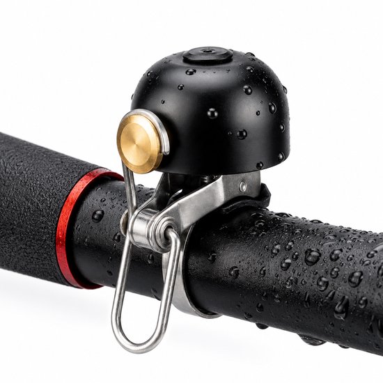 Zwarte fietsbel met gouden drukknop op een zwart stuur met waterdruppels.