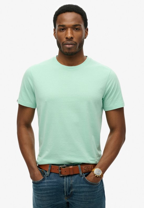 Homme portant un t-shirt Superdry vert menthe et un jean, mains dans les poches.