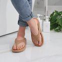 Persoon die beige slippers draagt op een witte tegelvloer.