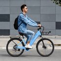 Man rijdt op een hemelsblauwe elektrische fiets met rugzak en denim jack.