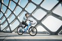 Vrouw rijdt op een hemelsblauwe elektrische fiets met een denim jack en helm.