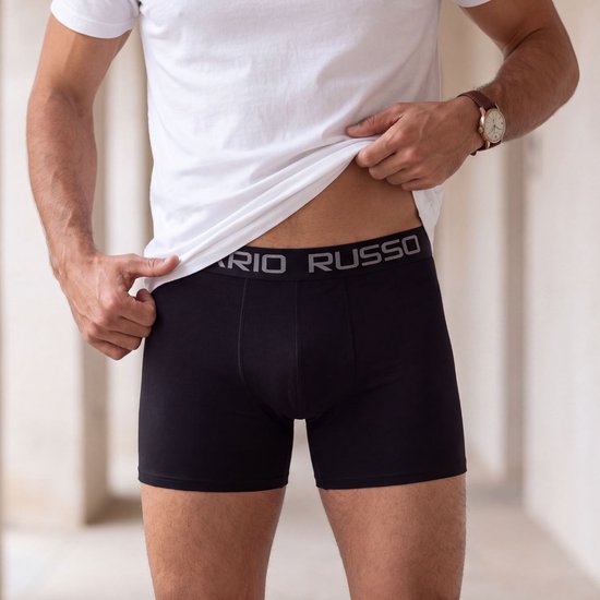 Een man met een witte t-shirt en zwarte Mario Russo boxershorts, met de tekst 'MARIO RUSSO' op de tailleband.