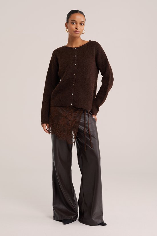 Model in bruin gebreid vest met knopen, bruine leren broek met kanten rokje.