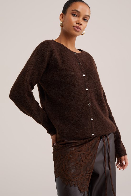 Bruin gebreid vest met knopen, gedragen door een model met gouden oorbellen.