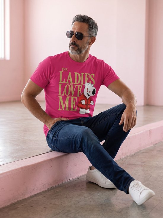 Man met zonnebril en spijkerbroek draagt een roze t-shirt met gouden tekst 'THE LADIES LOVE ME' en Brian Griffin met kusjes.