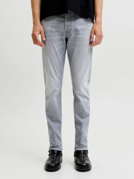 Man van voor, staand, in een lichtgrijze slim fit jeans en zwarte schoenen.