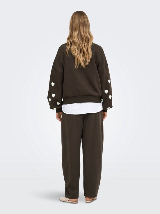 Achterkant van een donkerbruine sweater met witte hartjes op de mouwen, gedragen door een model.