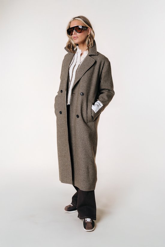 Mannequin dans un long manteau à carreaux brun et blanc, un pull blanc tricoté, un pantalon foncé et des lunettes de soleil.