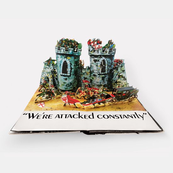Open boek met een pop-up kasteel, ridders en de tekst 'WE'RE ATTACKED CONSTANTLY'.