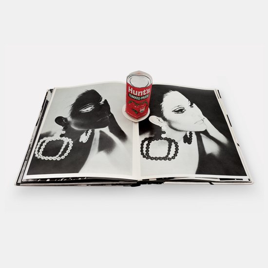 Open boek met op de pagina's een zwart-witfoto van een vrouw met grote oorbellen en een blikje tomatenpuree.