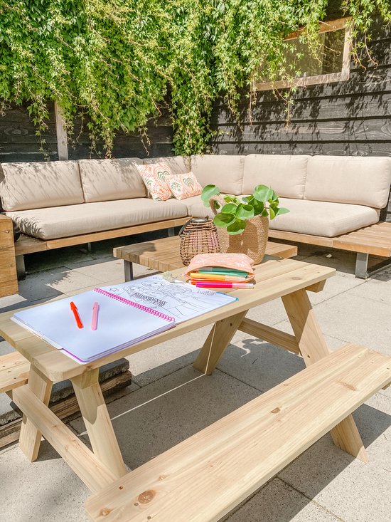 Houten picknicktafel met een opengetrokken kleurboek en stiften erop. In de achtergrond een loungebank.