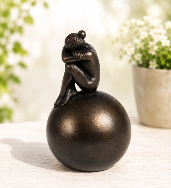 Petite figurine en bronze d'une fille aux cheveux relevés, assise sur un globe, tête sur les genoux, sur une table.