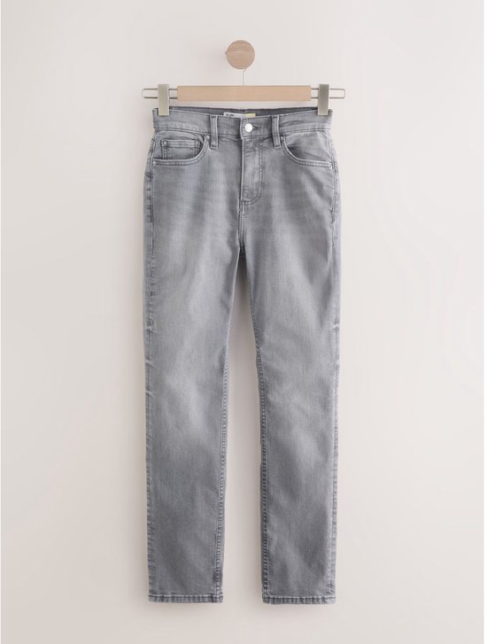 Een grijze jeans met halfhoge taille hangt aan een kledinghanger.