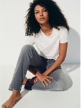 Model in een witte t-shirt en grijze jeans, zittend op de grond.