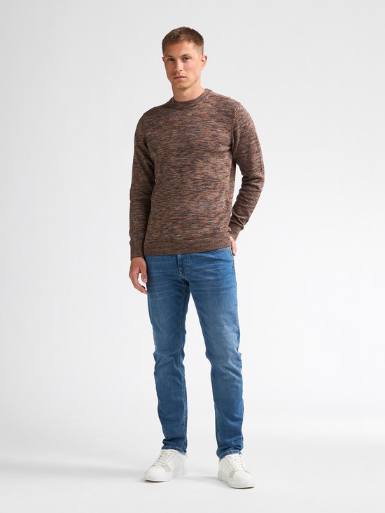 Man in een bruine gemêleerde trui met ronde hals, blauwe jeans en witte sneakers.