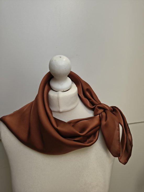 Bruine vierkante zijden sjaal, gedrapeerd om een paspop met een knoop aan de zijkant.