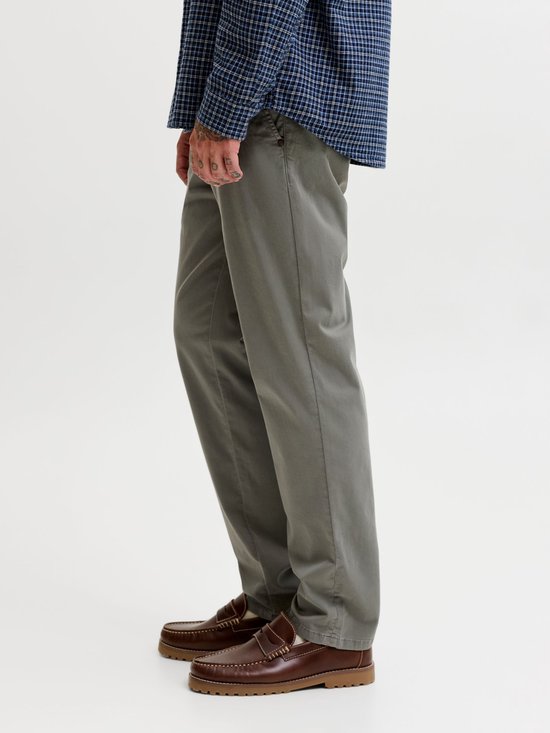 Man met grijze chino, draagt een blauw geruit overhemd en bruine loafers.