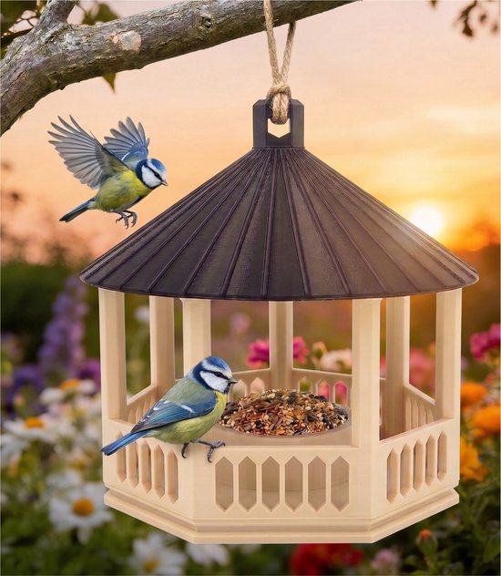 Zeshoekig vogelvoederhuis met crèmekleurig paviljoen en zwart dak. Twee blauwmeesjes, één vliegend, zijn bij het voer.
