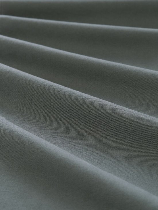 Textuurdetail van de donker olijfgroene stof van de chino, met zichtbare plooien.