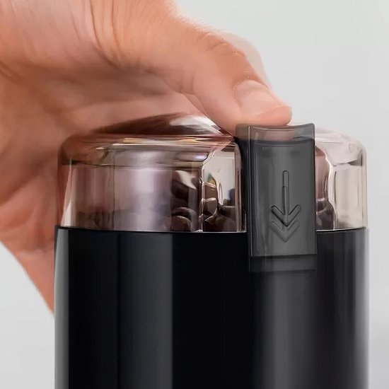Hand die de sluitclip van de doorzichtige deksel van een zwarte koffiemolen sluit.