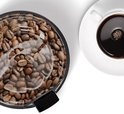 Zicht van bovenaf op een zwarte koffiemolen vol met koffiebonen, naast een kop koffie.