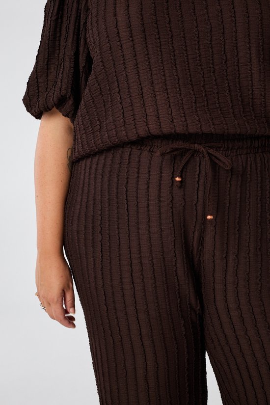 Detail van een bruine broek met trekkoord en koperen uiteinden.