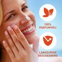 Vrouw met zonnebrandcrème op haar gezicht, met iconen van 100% parfumvrij en langdurige bescherming.