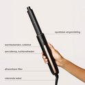 Hand die de zwarte MAE Airstyler II vasthoudt met gouden accenten en bedieningsknoppen. Labels geven delen aan: opzetstuk vergrendeling, warmtestanden, aan/uitknop, afneembare filter, roterende kabel.