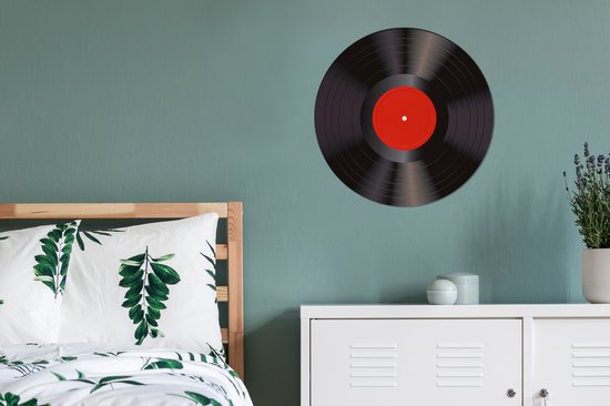 Zwarte vinyl LP met rood middellabel, hangend aan een muur boven een ladekast.