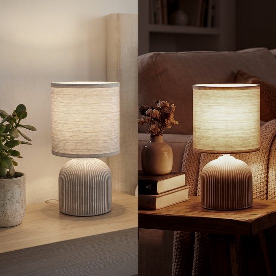 Lampe de table avec abat-jour en tissu et pied en céramique, à gauche dans une chambre lumineuse, à droite sur une table en bois dans une pièce sombre.