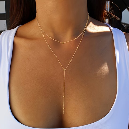 Een vrouw draagt een gouden dubbele ketting met balletjes en een Y-vormige hanger.