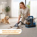 Een vrouw met een reinigingsmachine verwijdert hondenvlekken van een grijs tapijt, met een Golden Retriever ernaast.