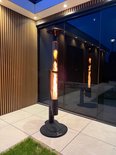 Zwarte staande terrasverwarmer met een glazen cilinder vol vlammen, bij een zwembad.