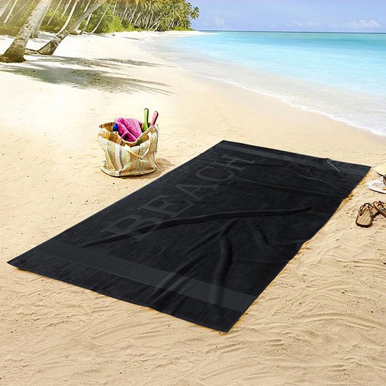 Zwarte strandhanddoek met de tekst 'BEACH' in reliëf, liggend op het zand.