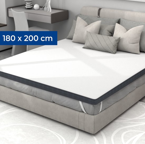 Un surmatelas blanc de 180 x 200 cm avec un bord rembourré gris foncé, sur un lit avec des coussins gris.