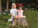 Meisje in tuin lacht en kijkt naar Luvibubs pop die uit roze pot groeit. Pop heeft roze haar en blaadjes.
