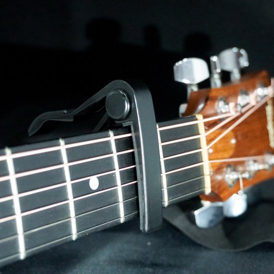 Zwarte gitaarcapo bevestigd op de fretten van een akoestische gitaar.