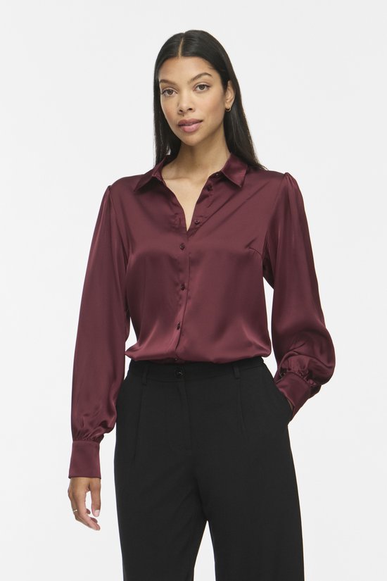 Model draagt bordeauxrode satijnen blouse met lange pofmouwen, kraag en knoopsluiting.