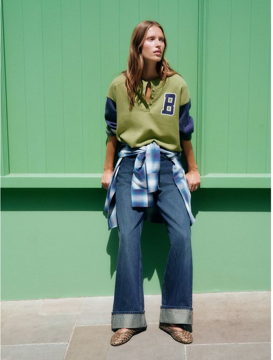 Model in een boyfriend jeans met omgeslagen pijpen, een groen shirt en een gebloemd geruit overhemd om de heupen.