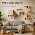 Kattenklimmuur in beige stof, geïnstalleerd boven een grijze bank. Drie katten zijn op de klimmuur, een klimt op een plateau, een loopt over de brug, een zit op de krabpaal.
