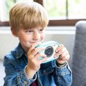 Jongetje met blond haar in een spijkerjasje houdt een cyaan Kidycam vast.