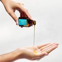 Een hand giet Moroccanoil Treatment olie in de andere hand.